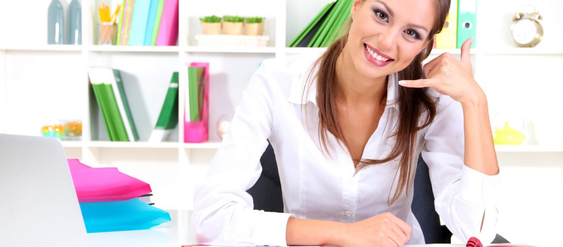 Young pretty business woman with phone and notebook working at office. Contact us